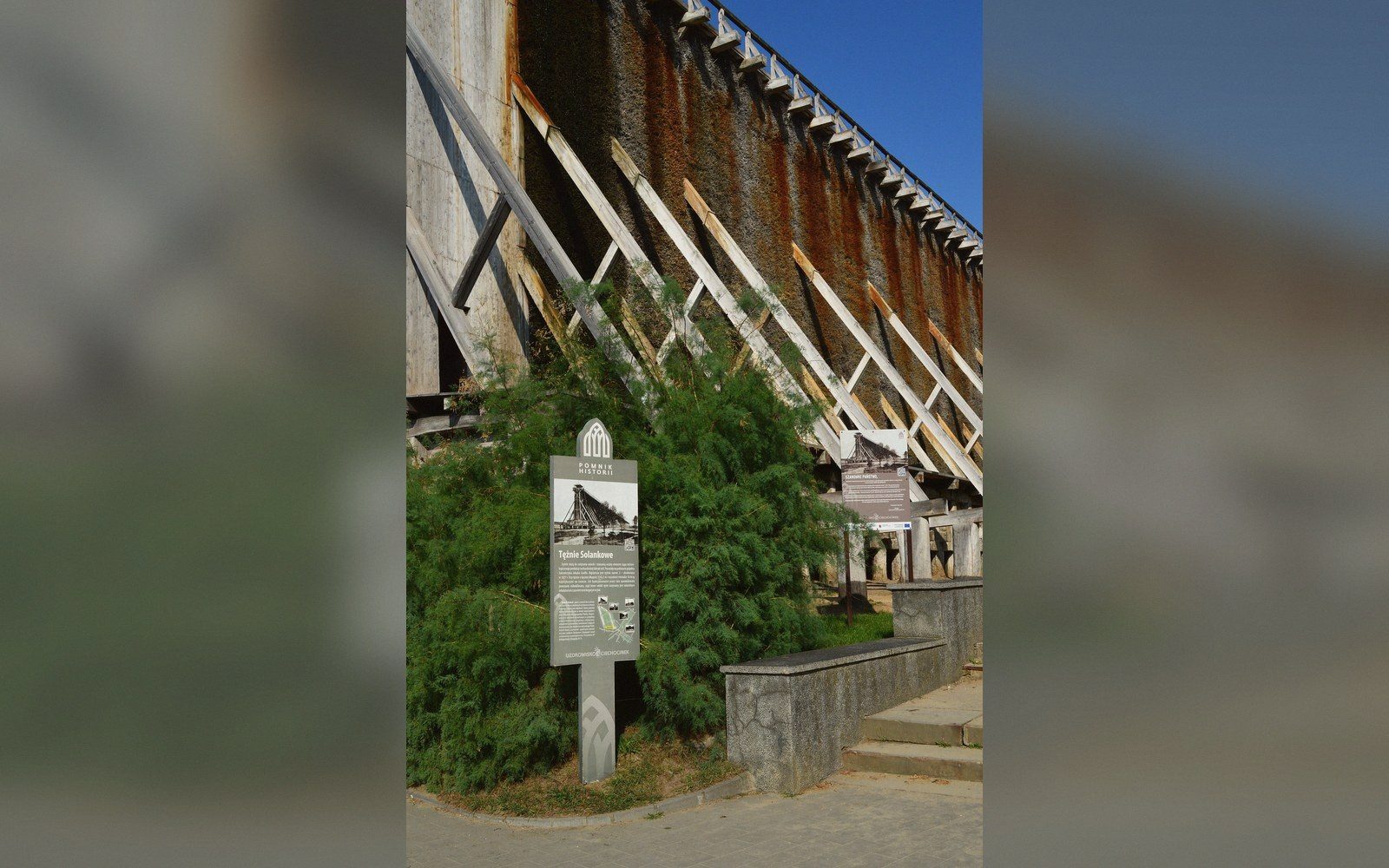 Wooden graduation tower with diagonal support beams and an informational sign beside a path