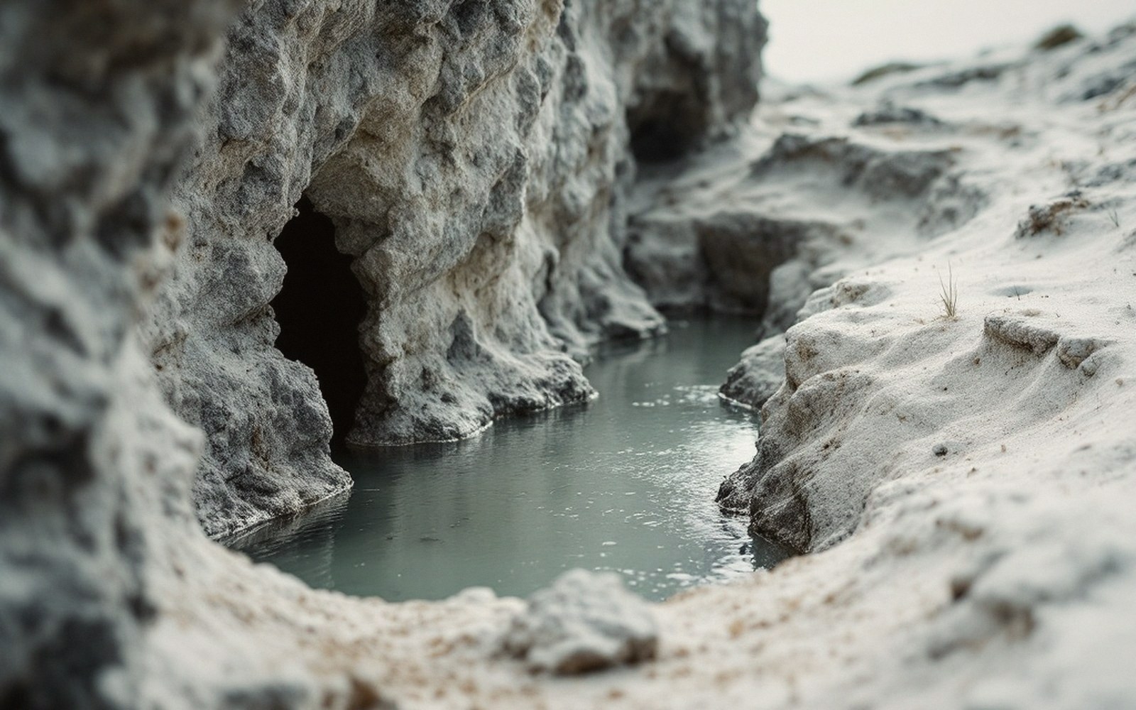 Small cave opening beside a still pool of brine amid weathered white rock