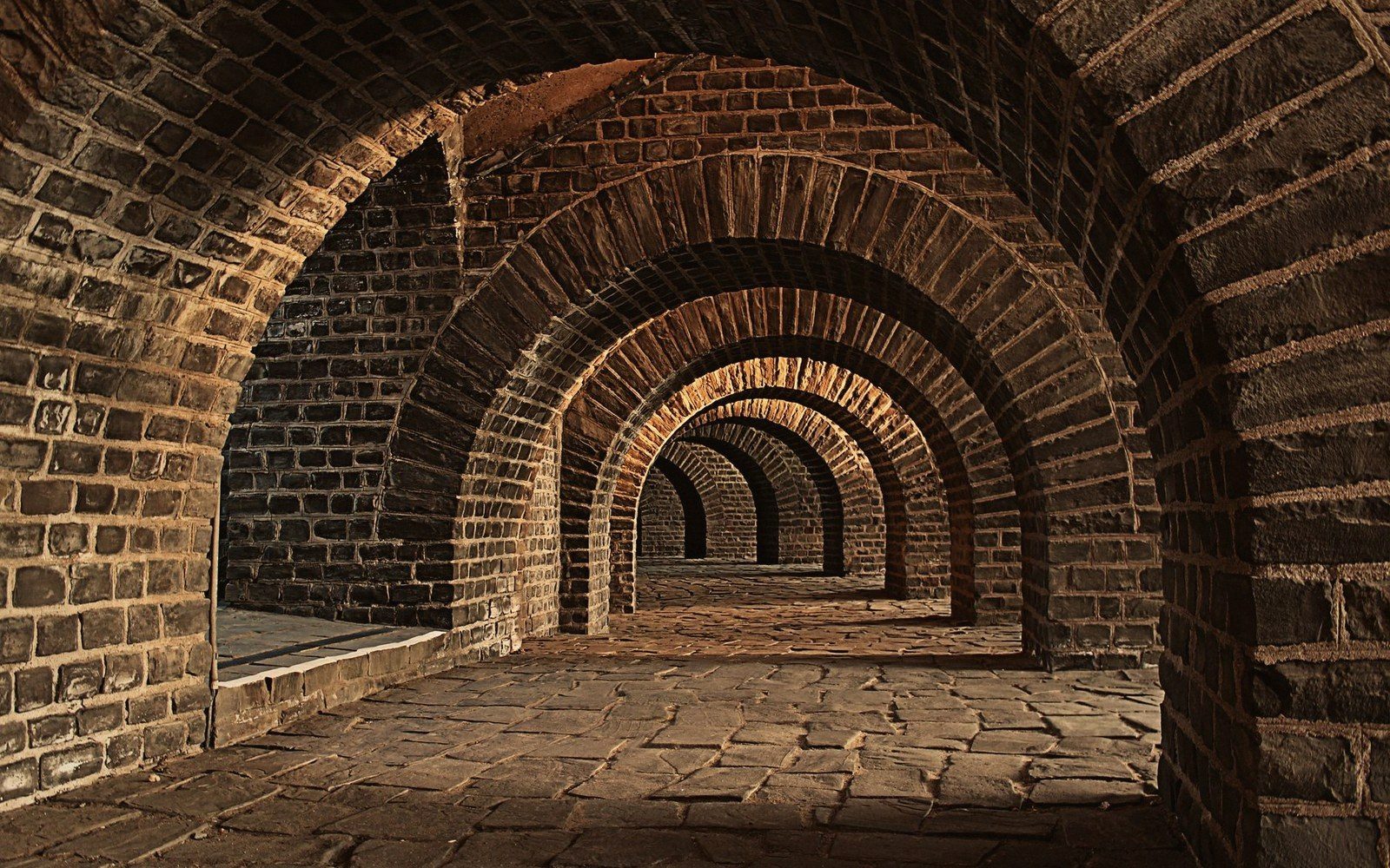 Repeating brick archways form a vaulted underground cellar with a stone floor