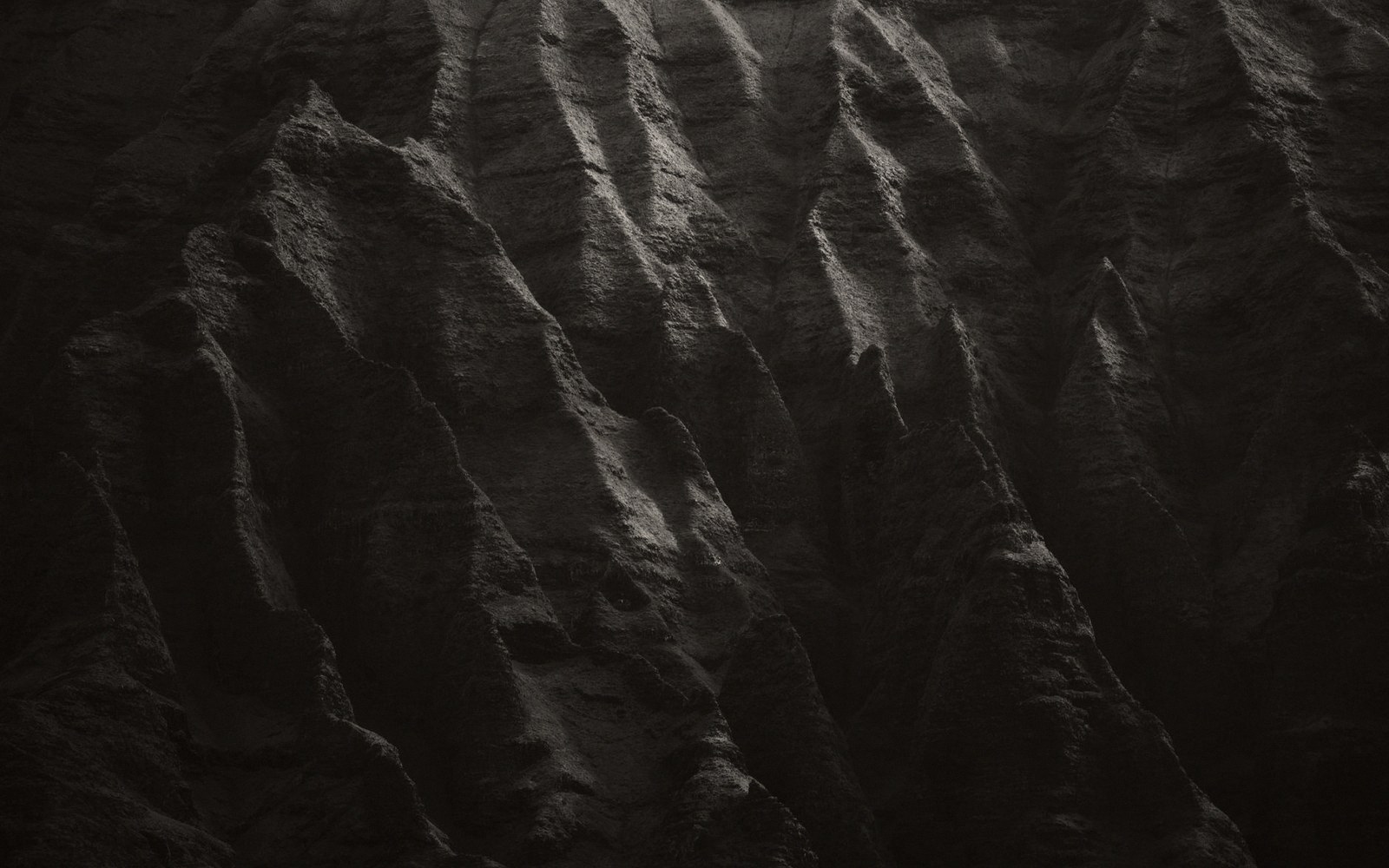 Sharp jagged ridgelines cast deep shadows across a dark eroded mountainside