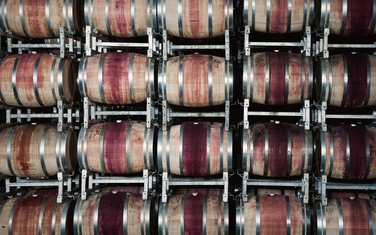 Rows of wine-stained oak barrels stacked on metal racks in a cellar